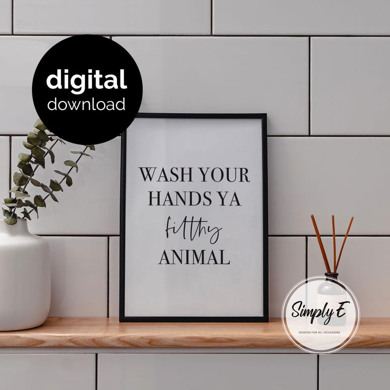 May include: A black framed wall art print featuring the white text WASH YOUR HANDS YA filthy ANIMAL in a mix of serif and script fonts. The print is displayed on a wooden shelf next to a white vase with greenery and a reed diffuser bottle.