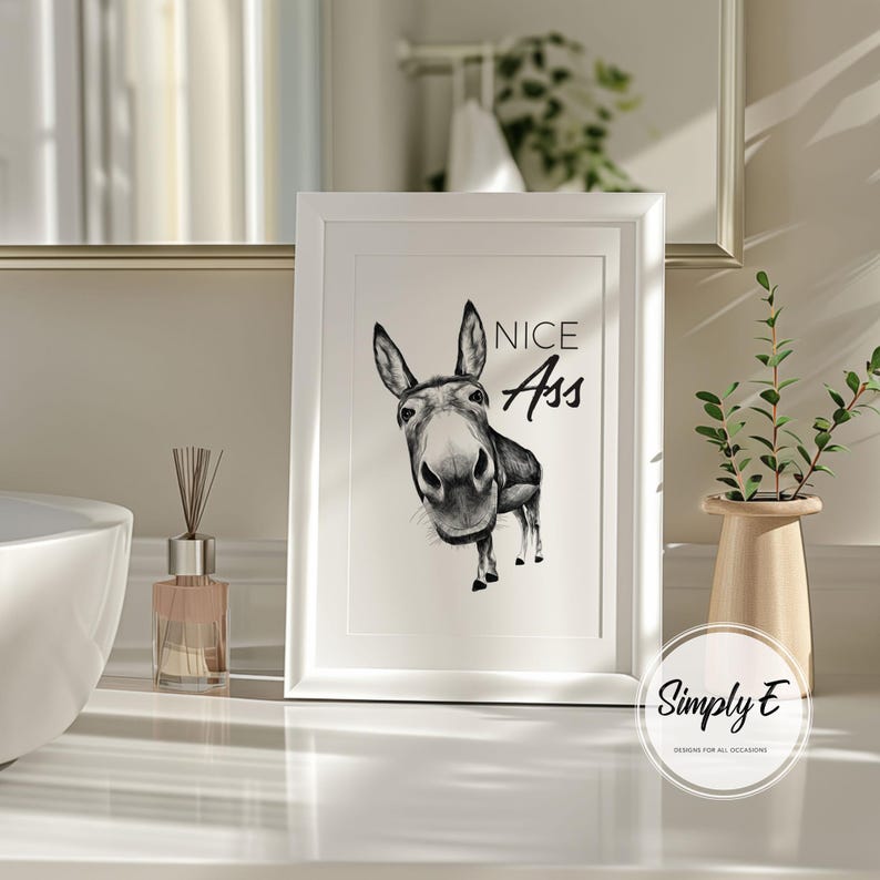 May include: A framed black and white print featuring a donkey illustration with the text "NICE Ass". The artwork is in a white frame and is displayed on a white surface. The print is a humorous piece of wall decor.