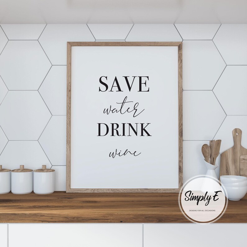 May include: A framed print with the words "SAVE water DRINK wine" in black script. The print has a light wood frame and is displayed on a wooden countertop. White hexagon tiles are in the background.