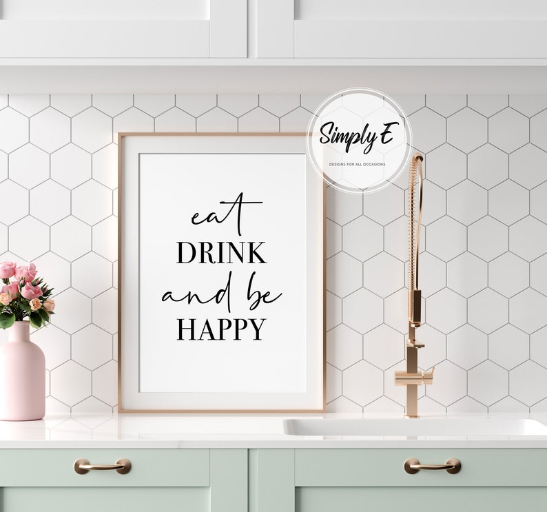 Peut inclure: Une impression encadr&eacute;e blanche avec le texte "eat DRINK and be HAPPY" en &eacute;criture cursive noire. L'impression est accroch&eacute;e &agrave; un mur blanc avec un motif de carreaux hexagonaux blancs.