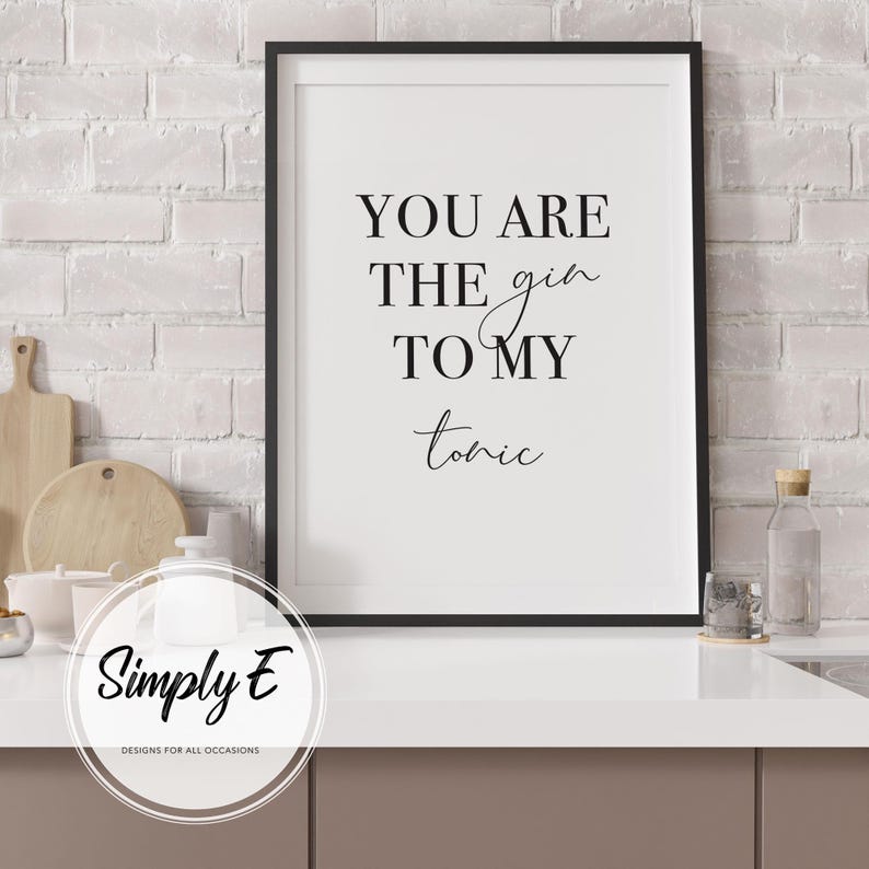 Puede incluir: Una impresi&oacute;n enmarcada con el texto "YOU ARE THE gin TO MY tonic" en escritura negra. La impresi&oacute;n est&aacute; en un marco negro y se muestra sobre una encimera blanca. El fondo es una pared de ladrillo blanco.