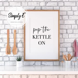 Peut inclure: Une impression encadr&eacute;e blanche avec du texte noir qui dit "pop the kettle on" sur un fond de mur en brique blanche.