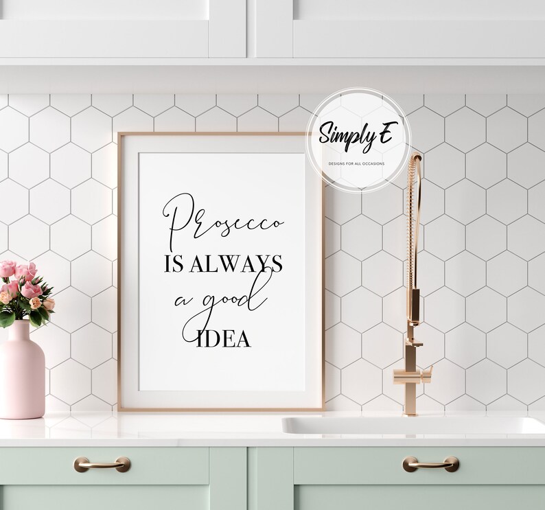 Op de afbeelding: Een witte ingelijste print met zwarte tekst die "Prosecco is always a good idea" luidt. De print hangt aan een witte muur met een wit zeshoekig tegelpatroon. Een ros&eacute;gouden kraan is zichtbaar op de achtergrond.