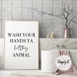 Puede incluir: Impresi&oacute;n enmarcada con el texto "WASH YOUR HANDS YA filthy ANIMAL" en negro. La impresi&oacute;n est&aacute; en un entorno de ba&ntilde;o con una ba&ntilde;era blanca, velas y un jarr&oacute;n decorativo. Decoraci&oacute;n de ba&ntilde;o humor&iacute;stica.