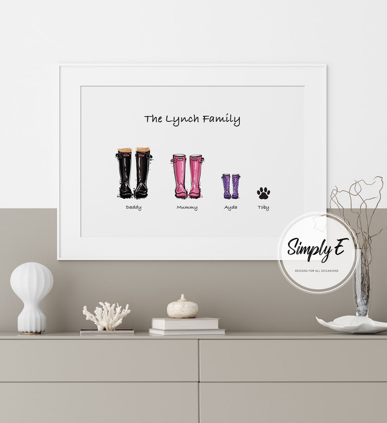 May include: A white framed print with the text "The Lynch Family" at the top.  Below the text are four pairs of rain boots, two black, two pink, and one purple.  The boots are labelled "Daddy", "Mummy", "Ayla", and "Toby".  The print is on a white background and has a white border.