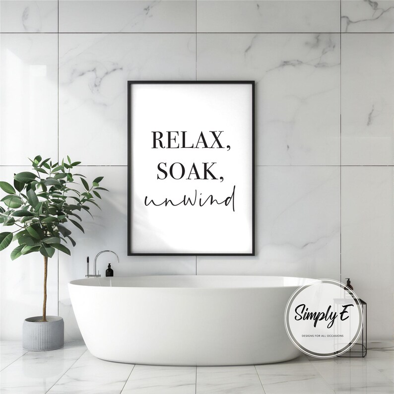 May include: A minimalist bathroom scene featuring a white bathtub, a framed print with the words "RELAX, SOAK, unwind," and a potted plant. The print is in a black frame. The bathroom has white marble-like tiles.