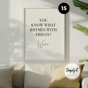 May include: A rectangular wall art print in a white frame featuring the black text YOU KNOW WHAT RHYMES WITH FRIDAY? Wine. The background of the print is a light cream colour. The design is displayed on a wall above a sofa with cushions.