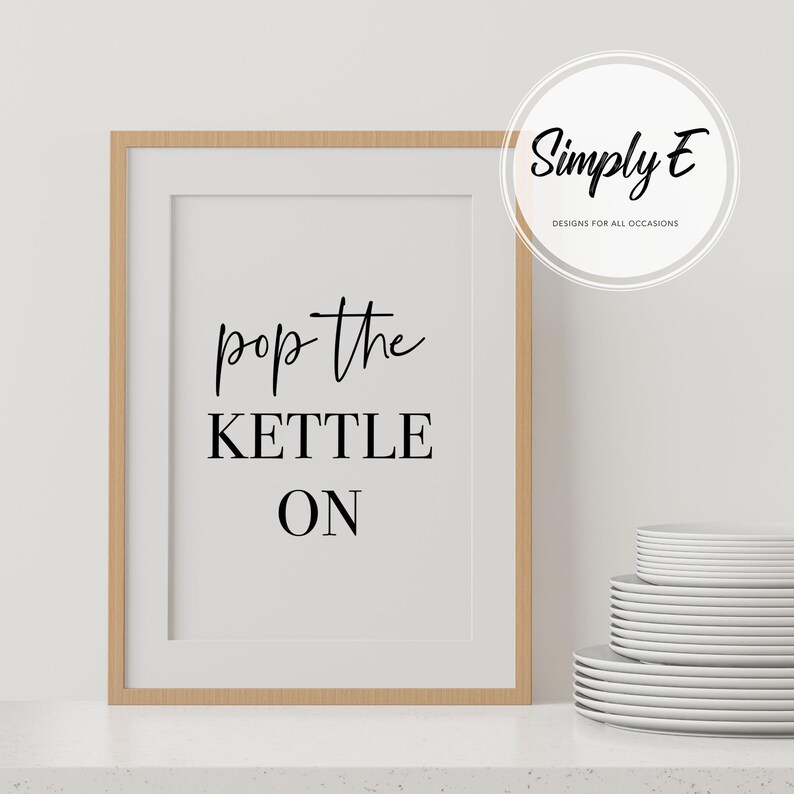 Peut inclure: Une impression encadr&eacute;e avec le texte "pop the kettle on" en lettres noires sur fond blanc. Le cadre est en bois brun clair.