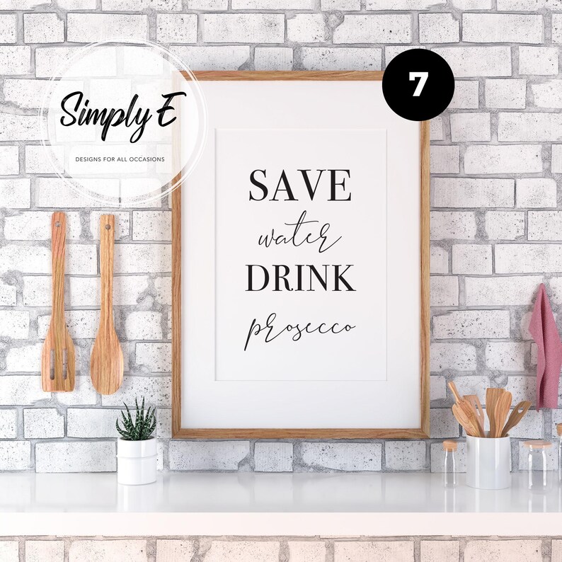 May include: A framed wall art print featuring the black text SAVE water DRINK Prosecco on a white background. The frame is light brown wood. The print is displayed in a kitchen setting with wooden utensils and a small potted succulent plant.