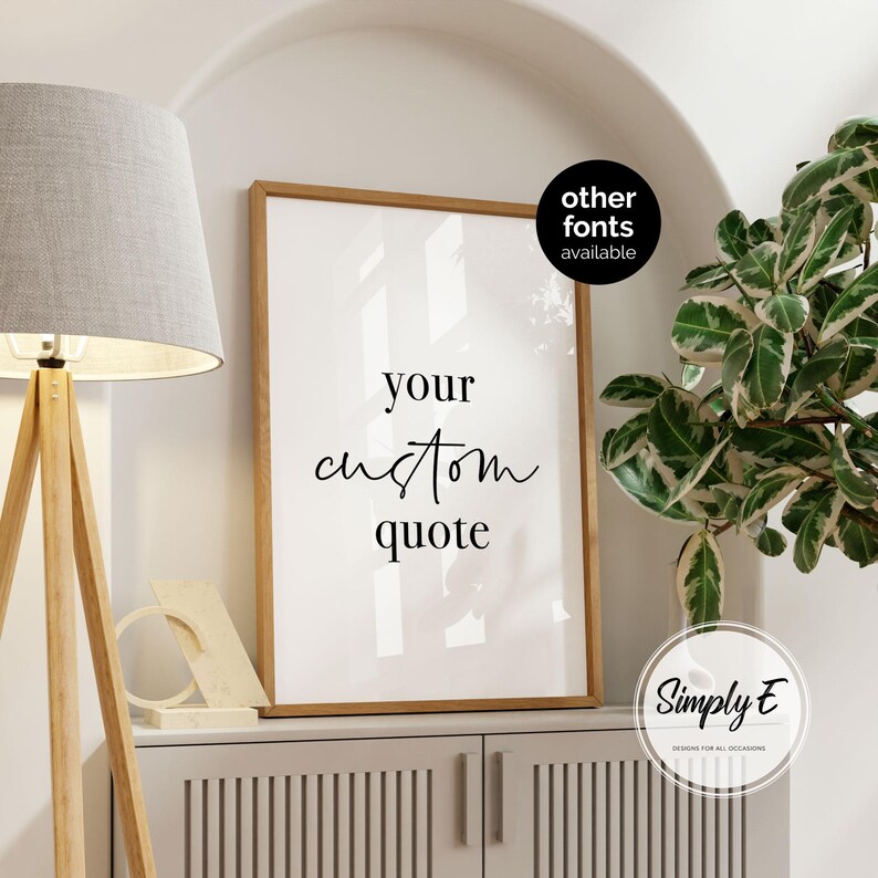 K&ouml;nnte beinhalten: Ein gerahmter Druck mit dem Text "your custom quote" in eleganter Schrift. Der Holzrahmen umgibt einen wei&szlig;en Hintergrund. Eine Lampe mit grauem Schirm und ein dekoratives Objekt befinden sich auf einem Schrank darunter. Die Worte "other fonts available" stehen in einem schwarzen Kreis.
