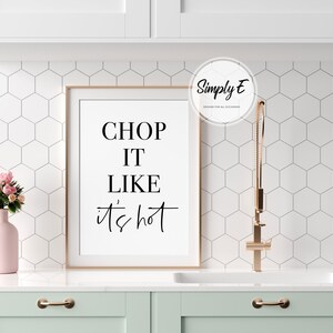 May include: A framed kitchen print with the text "CHOP IT LIKE IT'S HOT" in black lettering on a white background. The print is hanging on a white tiled wall above a light green cabinet.