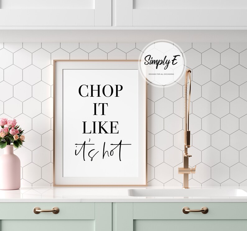 May include: A framed kitchen print with the text "CHOP IT LIKE IT'S HOT" in black lettering on a white background. The print is hanging on a white tiled wall above a light green cabinet.