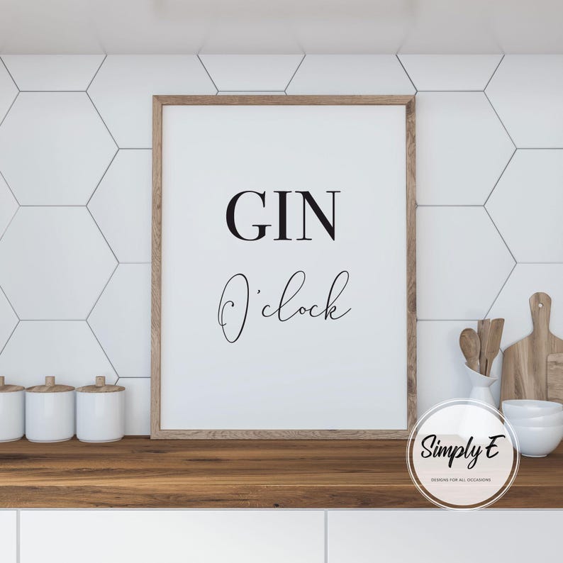 Puede incluir: Un cartel enmarcado con las palabras "GIN O'clock" en letras negras. El cartel tiene un marco de madera marr&oacute;n claro y se muestra sobre una encimera de madera. El fondo presenta baldosas hexagonales blancas.