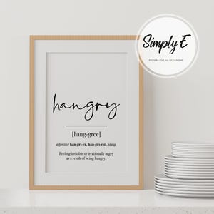 K&ouml;nnte beinhalten: Ein gerahmter Druck mit wei&szlig;em Hintergrund und schwarzem Text, der "hangry" lautet und das Wort als "sich gereizt oder irrational w&uuml;tend f&uuml;hlen, weil man hungrig ist" definiert.