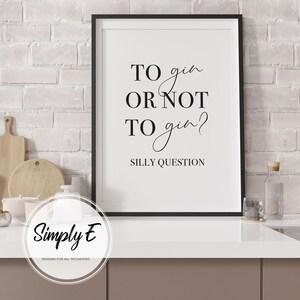 Pu&ograve; includere: Una stampa incorniciata nera con il testo "TO gin OR NOT TO gin? SILLY QUESTION" in nero. La stampa &egrave; in una cornice nera ed &egrave; esposta su un piano di lavoro bianco. Lo sfondo include un muro di mattoni bianchi e accessori da cucina.