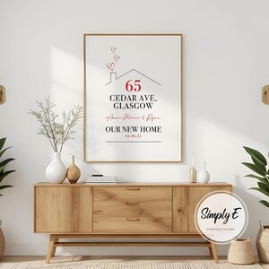 Peut inclure: Impression encadr&eacute;e avec le texte "65 Cedar Ave, Glasgow" et "Our New Home" en noir et rouge. Le design comprend un contour de maison avec des c&oelig;urs au-dessus. L'impression est affich&eacute;e sur un meuble en bois.