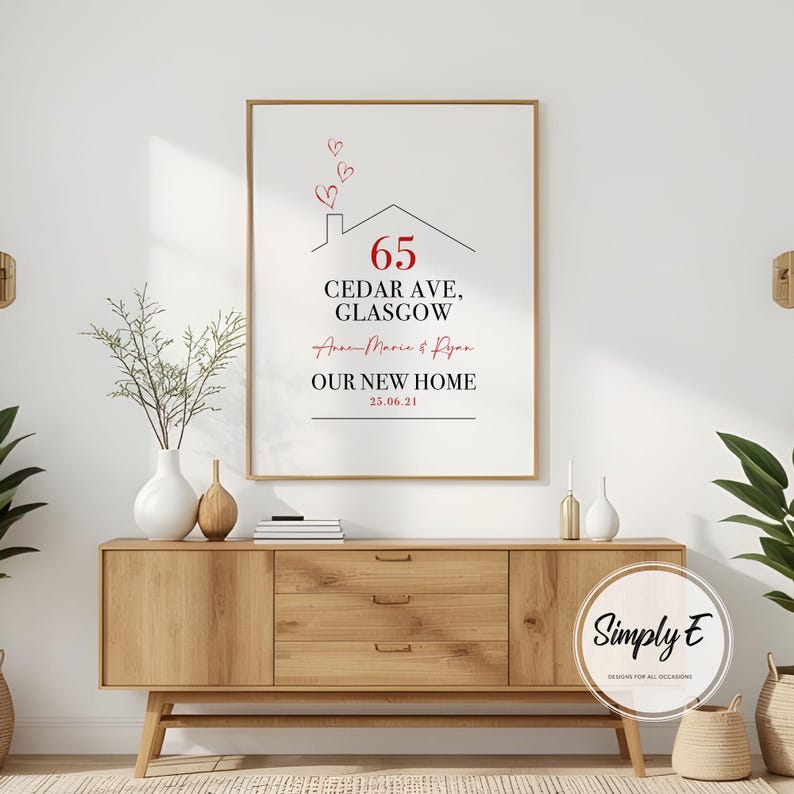 Peut inclure: Impression encadr&eacute;e avec le texte "65 Cedar Ave, Glasgow" et "Our New Home" en noir et rouge. Le design comprend un contour de maison avec des c&oelig;urs au-dessus. L'impression est affich&eacute;e sur un meuble en bois.
