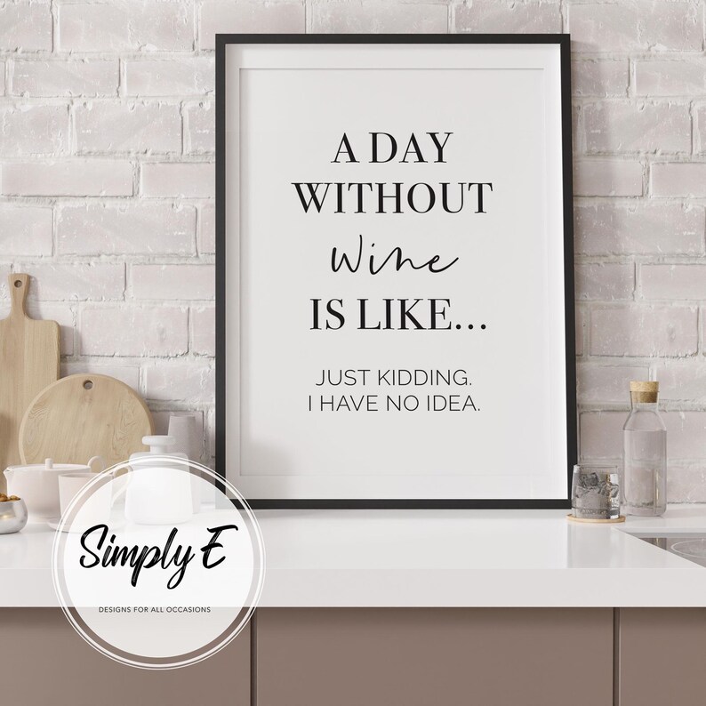 May include: Black framed print with the text "A DAY WITHOUT Wine IS LIKE... JUST KIDDING. I HAVE NO IDEA." The print is on a white background. The print is in a kitchen setting.