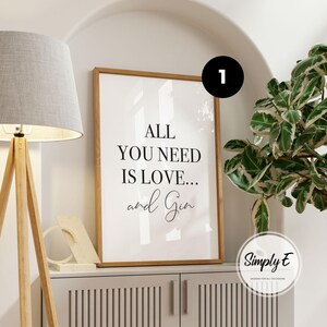 May include: A rectangular wall art print in a light wood frame featuring the black text ALL YOU NEED IS LOVE... and Gin on a white background. The print is displayed in a vertical orientation with a clean, simple design and clear typography.