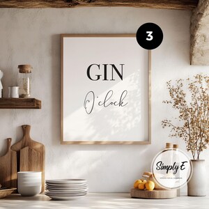 May include: A rectangular wall art print in a light wood frame featuring the black text GIN O'clock on a white background. The print includes a black circular icon with the number 3 in the top right corner and a Simply E logo in the bottom right.