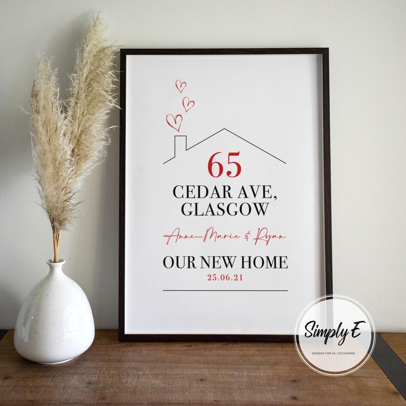 Peut inclure: Impression encadr&eacute;e avec un cadre noir. Elle pr&eacute;sente un dessin de maison, le num&eacute;ro 65 en rouge, et le texte "CEDAR AVE, GLASGOW". Elle comprend &eacute;galement des noms, "NOTRE NOUVELLE MAISON" et une date. Des c&oelig;urs rouges sont au-dessus.