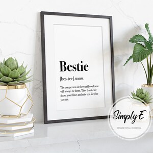 May include: A black framed print with the word "Bestie" defined as "the one person in the world you know will always be there. They don't care about your flaws and take you for who you are." The print is sitting on a white shelf with two potted plants.