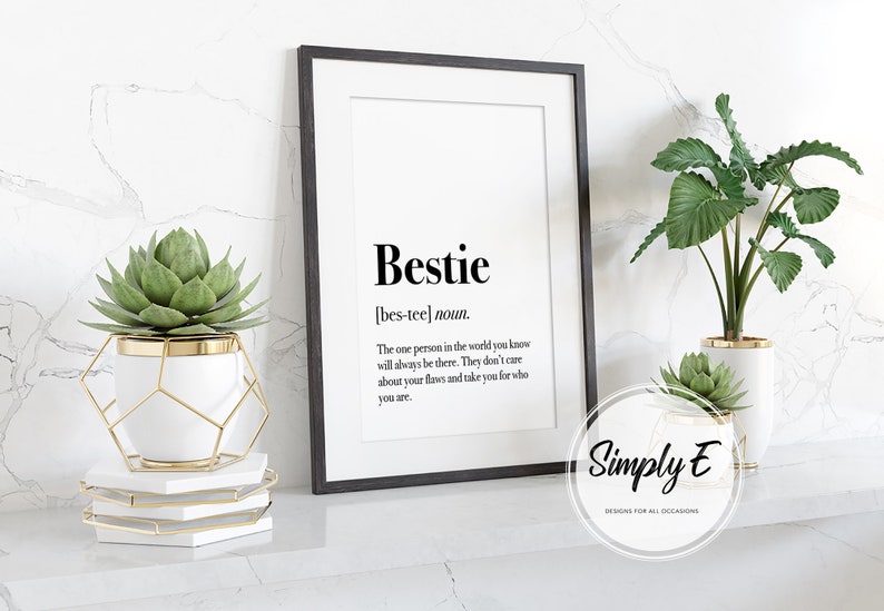 May include: A black framed print with the word "Bestie" defined as "the one person in the world you know will always be there. They don't care about your flaws and take you for who you are." The print is sitting on a white shelf with two potted plants.