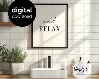 May include: A black framed wall art print featuring the text and relax in a combination of script and serif fonts on a cream background. The print is displayed above a white rectangular bathroom sink with a black faucet and two potted plants.