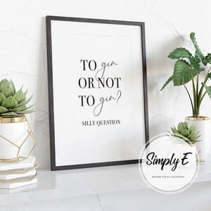 Pu&ograve; includere: Una stampa incorniciata con il testo "TO gin OR NOT TO gin? SILLY QUESTION" in nero. La stampa &egrave; in una cornice nera ed &egrave; esposta su una superficie bianca con piante in vasi bianchi e dorati.