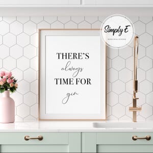 Puede incluir: Una impresi&oacute;n enmarcada con el texto "THERE'S always TIME FOR gin" en escritura negra. La impresi&oacute;n est&aacute; en un marco dorado, sobre un fondo blanco. Tambi&eacute;n se ve un jarr&oacute;n rosa con flores y un grifo dorado.