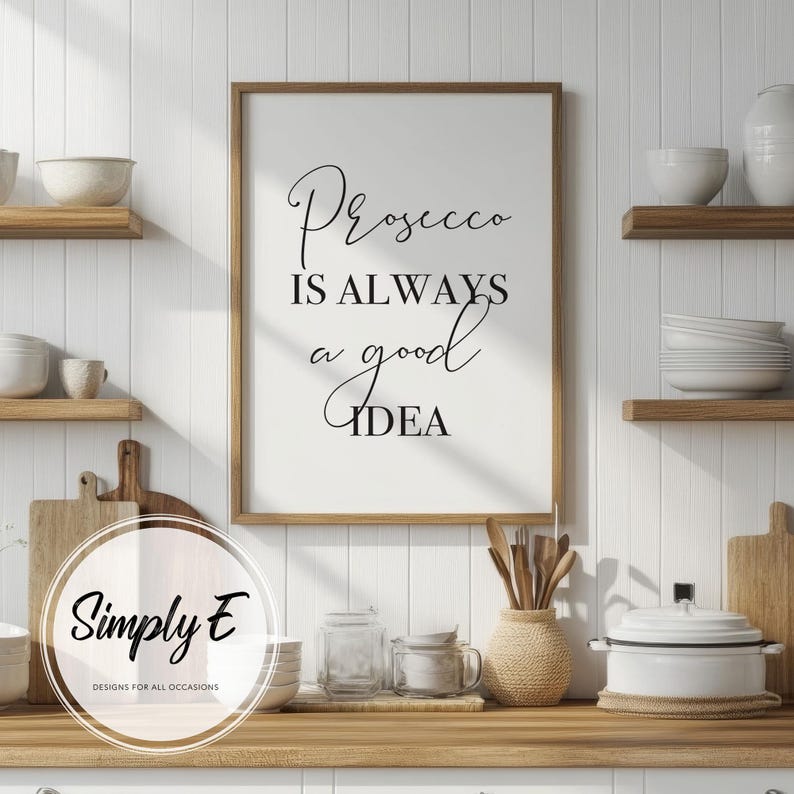 Op de afbeelding: Een zwart-witte printbare wanddecoratie met de tekst "Prosecco is always a good idea". Het bord is ingelijst in een zwart frame en hangt aan een witte muur in een keukenomgeving.