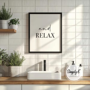 Puede incluir: Un cuadro negro con las palabras "and RELAX" en negro. El cuadro est&aacute; montado en una pared de azulejos blancos, encima de un lavabo blanco y una encimera de madera. Se ven plantas en macetas.