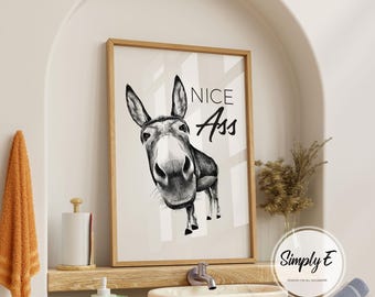 May include: A framed black and white print featuring a donkey with the text "NICE Ass". The artwork is displayed in a bathroom setting, with a wooden frame and a neutral colour palette.