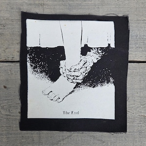 May include: Black and white patch featuring a stylized illustration of a foot and ankle bound by chains. The text "The End" is printed below the image. The patch is rectangular with a black border.