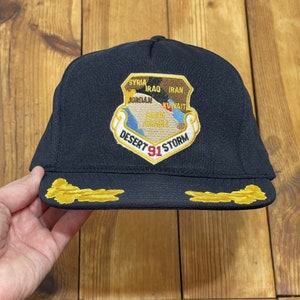 May include: A black baseball cap with a gold embroidered patch featuring a map of the Middle East and the text "Desert Storm 91".