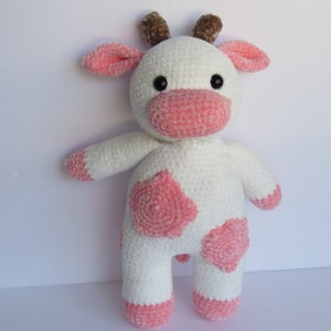 May include: A white crocheted plush cow toy with pink spots and brown antlers. The cow has a pink nose and black eyes.