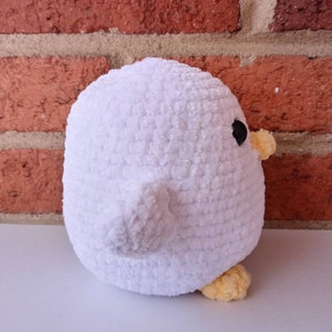 Puede incluir: Juguete de peluche blanco de ganchillo con forma de pollito con patas amarillas y un ojo negro. El pollito est&aacute; de espaldas a la c&aacute;mara.