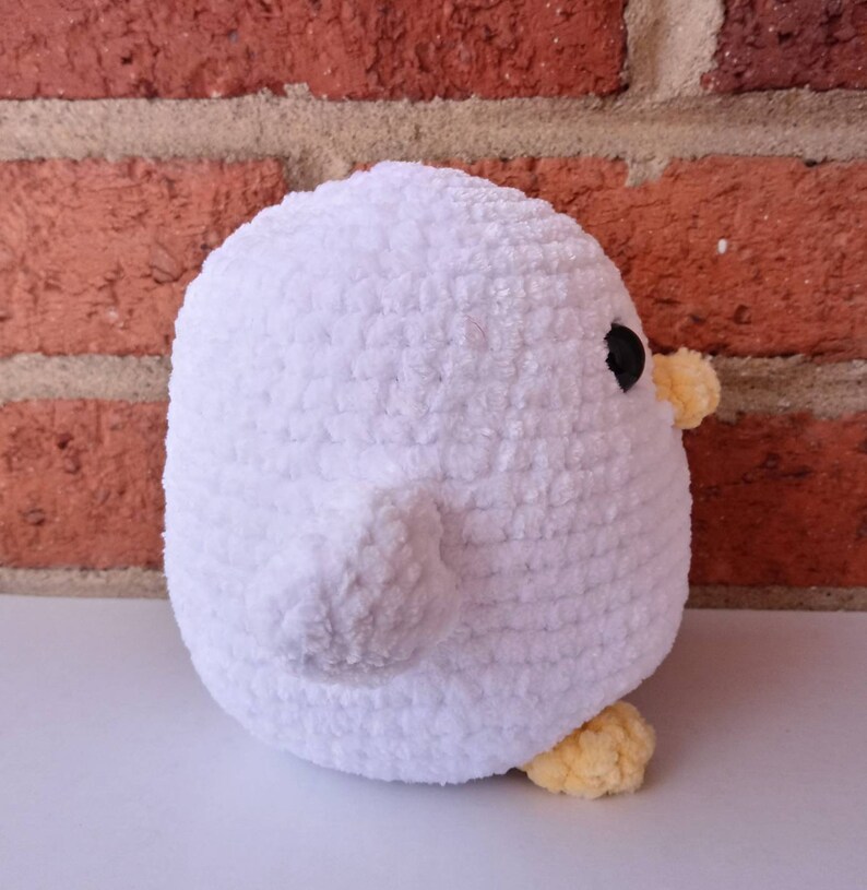 Puede incluir: Juguete de peluche blanco de ganchillo con forma de pollito con patas amarillas y un ojo negro. El pollito est&aacute; de espaldas a la c&aacute;mara.