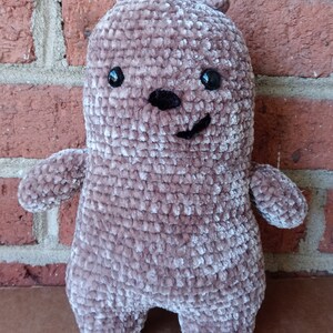 May include: A plush brown crocheted bear with black eyes and a black nose. The bear has a smiling expression.