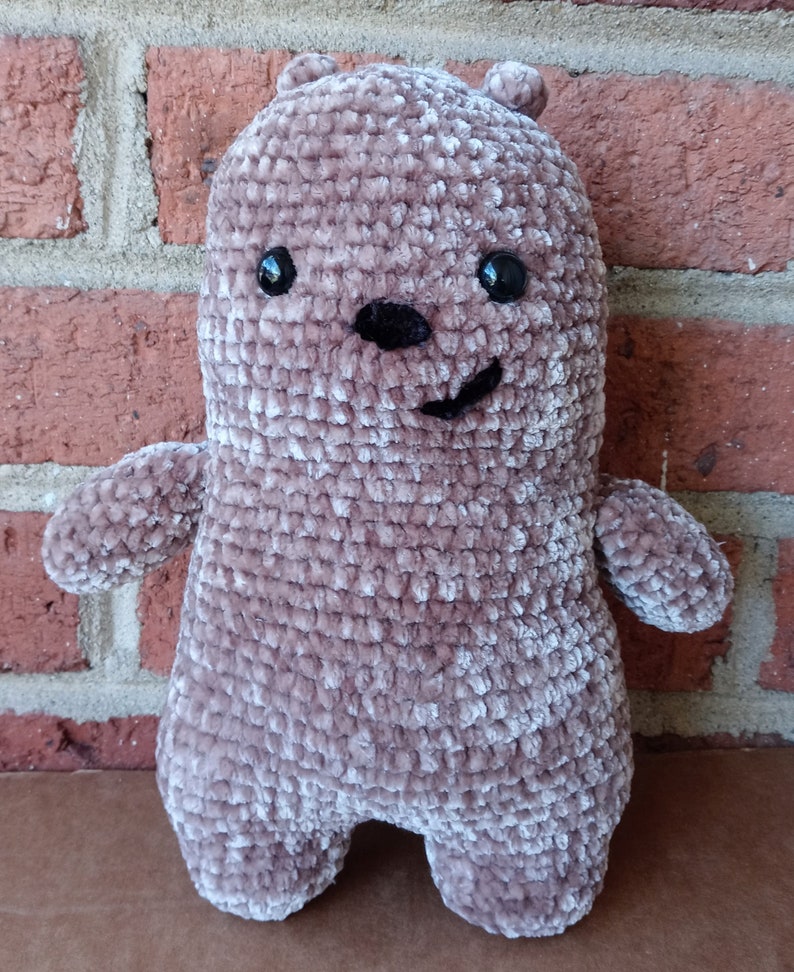 May include: A plush brown crocheted bear with black eyes and a black nose. The bear has a smiling expression.