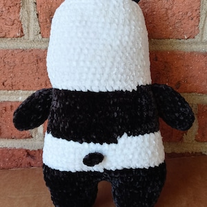 May include: A black and white crocheted panda plush toy. The panda has a white face and black ears, arms, legs, and a black patch around its eyes.