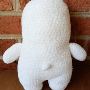 May include: White plush toy bear with a textured surface. The bear is standing on a brown surface.