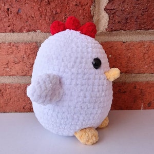 Puede incluir: Juguete de peluche de pollo blanco tejido a crochet con una cresta roja y patas amarillas. El juguete tiene ojos negros y un pico amarillo.
