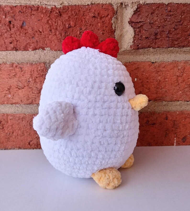Puede incluir: Juguete de peluche de pollo blanco tejido a crochet con una cresta roja y patas amarillas. El juguete tiene ojos negros y un pico amarillo.