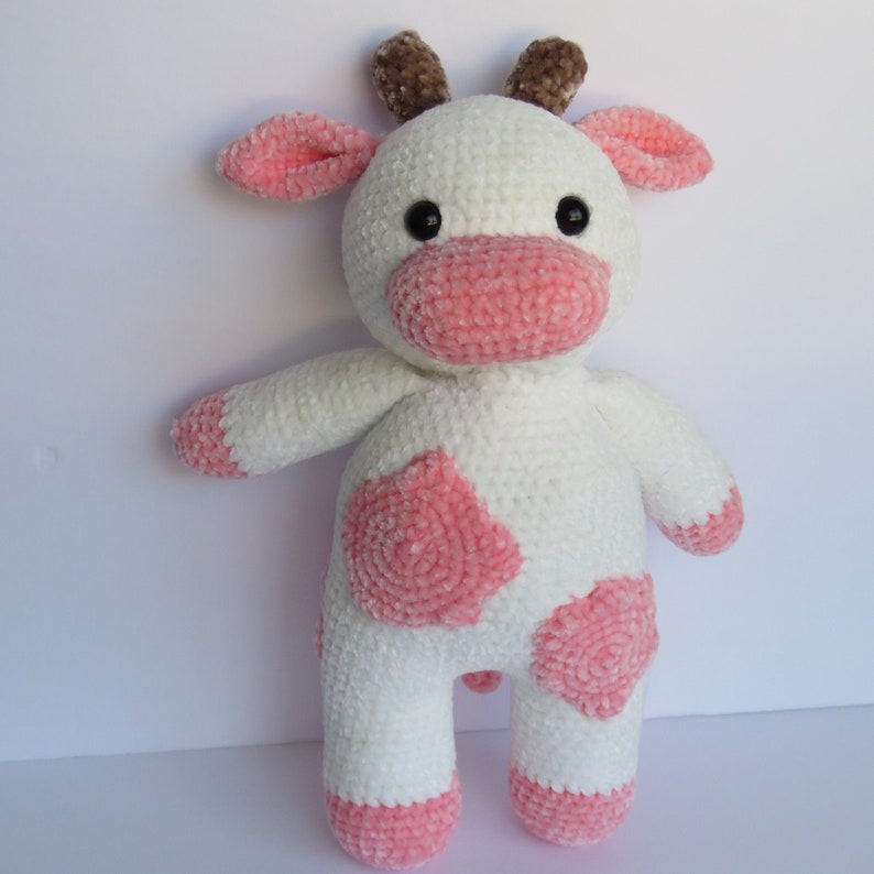 May include: A white crocheted plush cow toy with pink spots and brown antlers. The cow has a pink nose and black eyes.