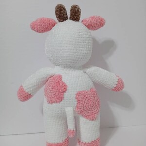 May include: A white crocheted cow plush toy with pink spots and brown horns. The toy has a pink tail.