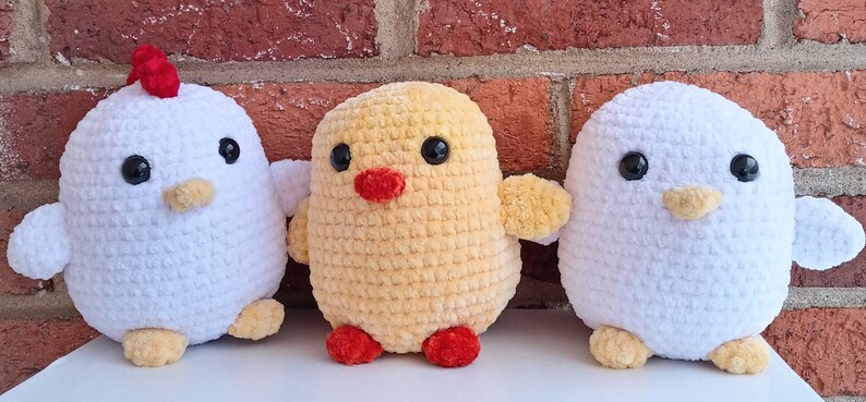 Puede incluir: Tres pollos de peluche tejidos a crochet. Uno es blanco con una cresta roja, otro es amarillo y el &uacute;ltimo es blanco. Todos tienen ojos negros y un peque&ntilde;o pico naranja.