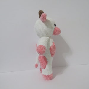 May include: A white crocheted cow plush toy with pink spots. The toy has a brown horn and black eyes.