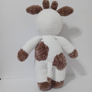 May include: A white crocheted plush toy cow with brown spots. The cow has a long tail and a brown crocheted head with ears.