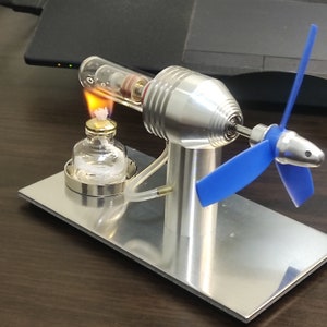 May include: A small, silver, model steam engine with a blue propeller. The engine is powered by a small flame from a glass fuel tank.